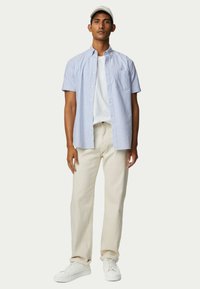 Korte mouwen, lichtblauw gestreept shirt over een wit T-shirt, gecombineerd met beige broeken en witte sneakers. Het shirt heeft een zak.