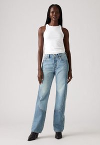 Hvit ribbet tanktopp og lyseblå vide jeans med falmede detaljer og søm på siden. Bært med svarte ankelstøvler med hæl.