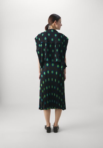 Black pleated dress with green and blue circular pattern, relaxed fit, short sleeves, and a hem that falls mid-calf. Paired with black shoes.