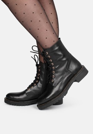 Botines de cuero negro con diseño de cordones, ojales dorados, cremallera lateral y suela de goma texturizada con tacón bajo.