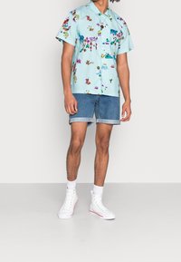 Camicetta azzurra a maniche corte con motivi floreali colorati, abbinata a pantaloni shorts di denim arrotolati e sneakers bianche alte.