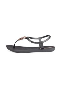 Black sandal with a flat sole, textured footbed, and T-strap design. Features a circular metallic accent at the front.