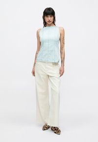 Top sin mangas azul claro con costuras verticales, combinado con pantalones anchos color crema y zapatos con estampado de leopardo. Diseño minimalista, textura suave.