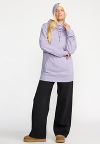 Sweat-shirt à capuche violet clair avec une poche kangourou et un cordon de serrage, associé à un pantalon large noir et des chaussures beige.