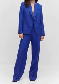 Veste bleue ajustée avec revers à pointe, fermeture à un bouton, et pantalons larges assortis en tissu texturé.