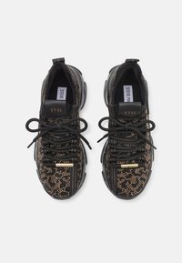 Black sneakers feature a textured pattern of gold studs, fabric and rubber accents, round laces, and a logo on the tongue and heel.