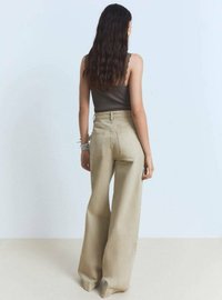 Jeans bej, cu picioare largi, din denim, cu talie înaltă și buzunare pe spate, asortați cu un top închis la culoare, pe un fundal deschis.