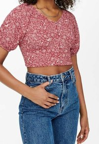Rote Bluse mit floralem Print, kurz geschnitten, mit kurzen Puffärmeln und V-Ausschnitt, kombiniert mit hochgeschnittenen blauen Jeans.