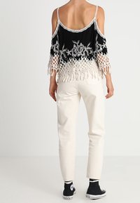 Haut noir épaules dénudées avec broderie florale blanche et détails en macramé, associé à un pantalon couleur crème et des baskets noires.