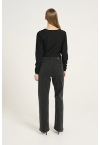 Schwarzes Langarmoberteil und hochgeschnittene dunkelgraue Jeans mit geradem Bein und dezenten Gesäßtaschen, aus einem glatten Material.