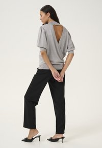 Haut métallique gris avec des manches bouffantes et un dos dénudé, associé à un pantalon noir et des mules à talons noirs. Texture lisse et design ajusté.
