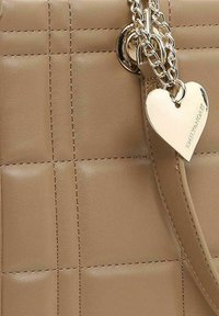 Sac en cuir synthétique beige avec un motif matelassé, doté d'accastillage en chaîne argentée et d'un charm en forme de cœur attaché à une sangle.