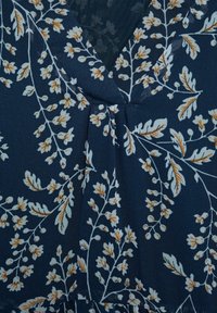 Námořnický náplet s jemným bílým a světle hnědým květinovým vzorem a skládacím detailem na výstřihu ve tvaru V.