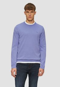 Lavenderfarbener Rundhals-Pullover, gestrickter Stoff, Rippbündchen und -saum, slim fit, Logo-Detail auf der Brust, getragen über einem weißen T-Shirt, kombiniert mit dunklen Jeans.