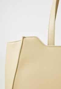 Sac fourre-tout en simili cuir jaune, avec une texture lisse, une forme structurée et des accents cousus. Doté d'une seule poignée et d'un design minimaliste.