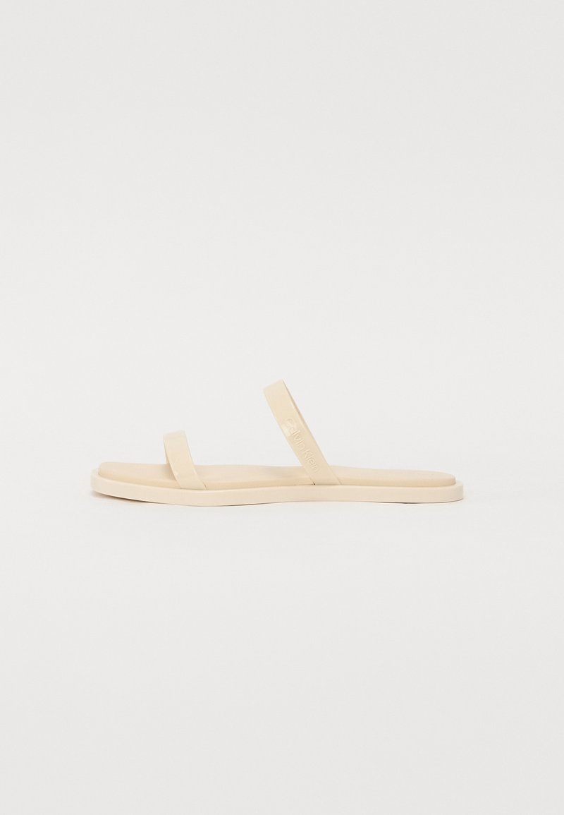 Beige flip-flop sandaler med minimalistisk design, der har to tynde stropper og en flad sål. Lavet af glat syntetisk materiale.