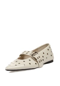 Zapato plano de cuero blanco con punta afilada, diseño recortado y tachuelas decorativas en plateado. Presenta una correa con una hebilla metálica.