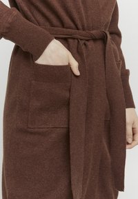 Brązowy sweter z dzianiny z paskiem, ribbowanymi mankietami i przednimi kieszeniami, o miękkiej teksturze i luźnym kroju.