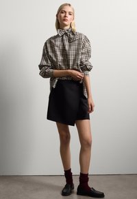 Plaid button-up shirt with tied collar, paired with a black asymmetrical skirt. Dark red socks and black loafers complete the outfit.