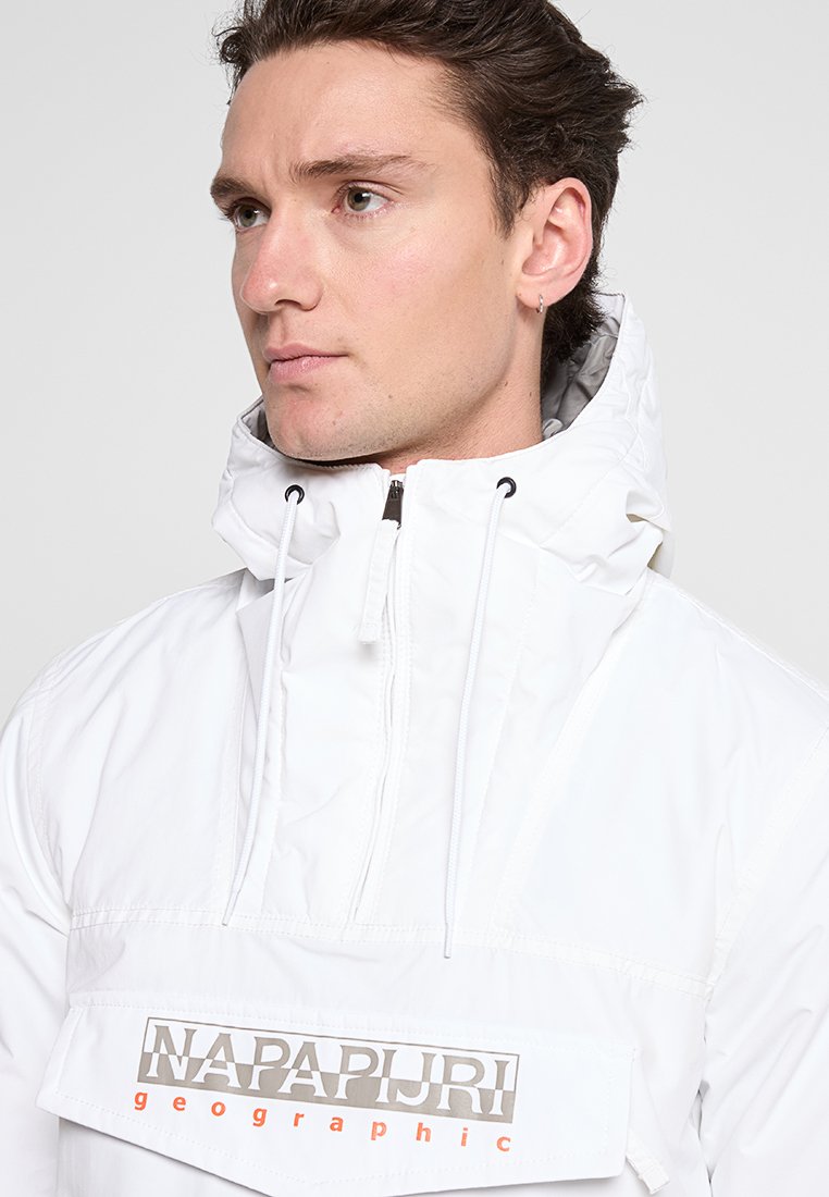 Giacca anorak bianca con zip frontale, cordini elastici sul cappuccio e una grande toppa con logo sul petto. Tessuto liscio e leggero.