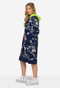 Robe à capuche bleu marine avec un imprimé abstrait blanc, poches kangourou et une capuche verte fluo contrastante. Fabriquée dans un tissu doux avec des poignets côtelés.