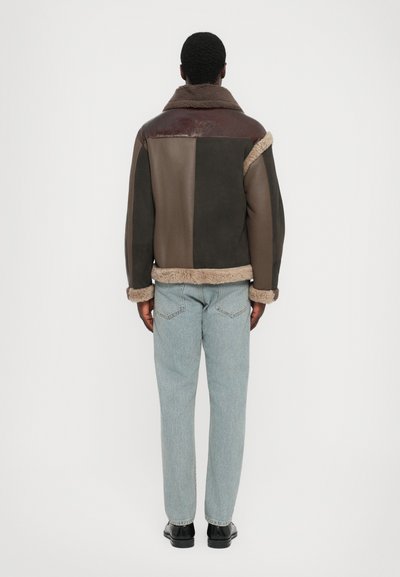Braune Jacke mit Schaffellfutter und unterschiedlich strukturierten Patches in Dunkelgrün, Braun und Burgunder. Sie verfügt über einen Stehkragen und weiche Ärmelabschlüsse.