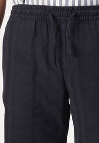 Donkerblauwe broek van gestructureerde stof met een elastische tailleband en verstelbaar trekkoord, voorzien van verticale naaddetails en zijzakken.