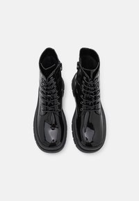 Bottines en cuir verni noir avec une semelle épaisse, dotées de lacets et d'œillets en métal. L'intérieur est doublé d'une matière douce pour plus de confort.