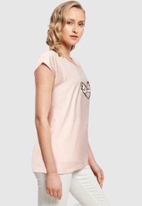 Lyserød bomulds T-shirt med korte ærmer, prydet med et hjerte-design i sort og beige, glat tekstur, afslappet pasform.