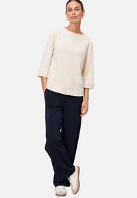 Pull à côtes crème avec un col bateau, manches trois-quarts, associé à un pantalon large marine et des baskets blanches. Design simple et décontracté.