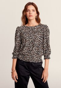 Blusa con stampa a leopardo realizzata in un tessuto morbido, scollo rotondo, maniche a tre quarti e orlo arricciato. Abbinata a pantaloni neri e a un bracciale.
