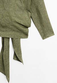 Vêtement olive avec une texture douce, présentant un avant drapé et un détail noué, mettant en avant un design moderne et élégant.