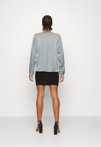 Blusa de cetim azul-claro de mangas longas com decote redondo, combinada com uma mini saia justa preta e sandálias de salto alto pretas.