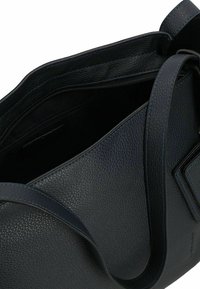 Sac en cuir noir à bandoulière avec une surface texturée, doté d'une fermeture éclair et d'une large sangle. L'intérieur est spacieux et sombre.