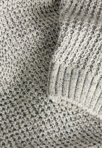 Strickstoff in Hellgrau mit dunklen Flecken, der eine strukturierte Webart und gerippte Akzente aufweist. Weiche und flexible Textur.