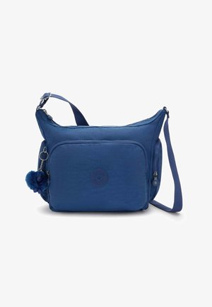 Sac bandoulière bleu en tissu léger, équipé d'une poche zippée à l'avant, d'un écusson logo et d'un pompon duveteux attaché à la fermeture éclair.