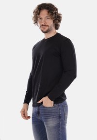 Maglietta a maniche lunghe nera in tessuto di cotone, con colletto tondo, texture liscia e silhouette aderente, indossata con jeans blu.