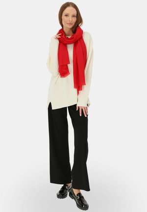 Słoniowa, dziana sweater z bocznymi rozcięciami, czarne szerokie spodnie, a także jasnoczerwona chusta z frędzlami, zestawione z błyszczącymi czarnymi mokasynami.