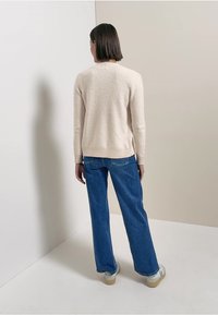 Pull beige texturé à manches longues, associé à un jean bleu clair à jambes larges et des baskets beigess. Vue de dos, sur fond neutre.