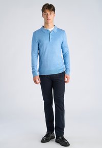 Jasnoniebieska koszulka polo z długim rękawem, kołnierzykiem i trzema guzikami, zestawiona z ciemnogranatowymi spodniami i czarnymi butami. Gładka faktura, dopasowany krój.