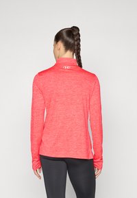 Röd långärmad träningsskjorta med hög krage, slät textur och kontrasterande logga på baksidan, kombinerad med svarta leggings.