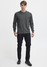 Suéter de punto gris con un cuello redondo, mangas largas, puños y dobladillo acanalados, combinado con pantalones negros y zapatos negros.
