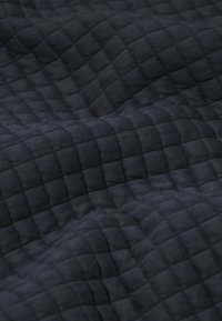 Tissu sombre avec un motif en relief de quadrillage matelassé formant des plis doux et ondulés ainsi qu'une surface texturée.