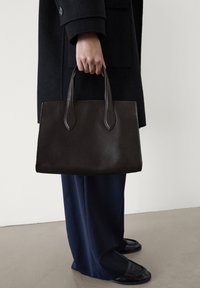 Bruine leren tote bag met verlengde hengsels, rechthoekige vorm, gladde textuur en minimalistisch ontwerp. Draagt bij navy broek.