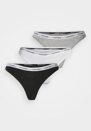 Três pares de tanga Calvin Klein nas cores preto, cinza e branco. Cada um apresenta uma cintura macia com texto do logótipo repetido. Material de algodão suave.
