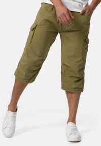 Shorts cargo kaki en mélange de coton, dotés de plusieurs poches latérales, d'une coupe longueur genou et d'ourlets retroussés. Stylés avec des baskets blanches.