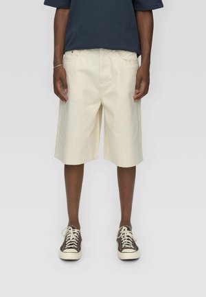 Beżowe szorty cargo o prostym kroju, wykonane z bawełny, z kieszeniami z przodu, zamkiem błyskawicznym i widocznymi detalami przeszyć.