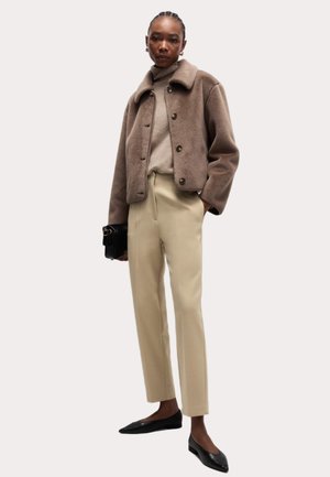 Veste en polaire marron avec un col et des boutons, associée à un pantalon beige ajusté et des ballerines noires, portant un sac à main noir.