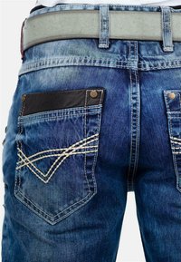 Jeans in denim blu sbiadito con una tasca nera a contrasto, caratterizzati da cuciture decorative a zigzag sulle tasche posteriori.