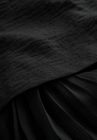 Tessuto nero con una superficie texturizzata, caratterizzato da uno strato superiore liscio e una sezione inferiore plissettata, entrambi in una tonalità di nero profondo e uniforme.